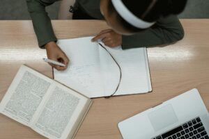 Top view of a person studying with an open book and laptop, writing notes in a notebook.
