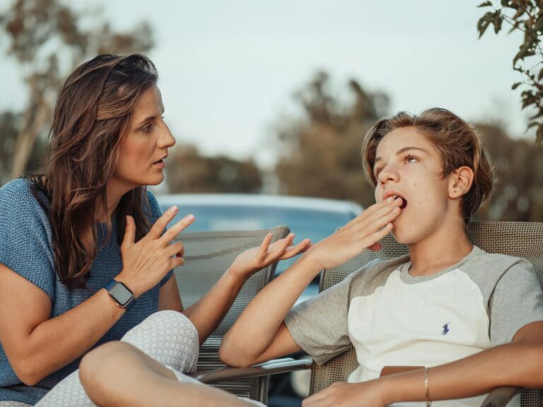 A mother and her teenage son are having a conversation outdoors. The son appears disinterested.