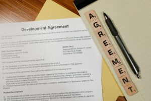 Close-up of a development agreement document with pen and Scrabble tiles spelling 'AGREEMENT.'