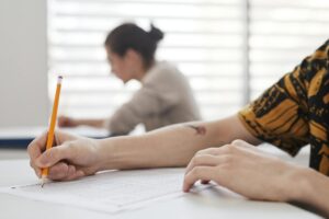 Close-up of student's hands writing on exam sheet, indoors with blurred background.