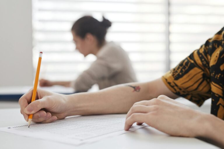 Close-up of student's hands writing on exam sheet, indoors with blurred background.